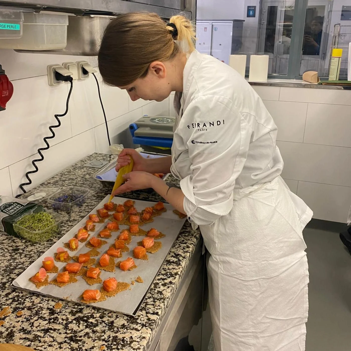 La pâtissière en tenue de chef Ferrandi, dressant des bouchées dans son atelier